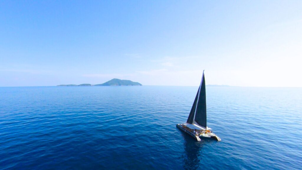 Barca a vela in mezzo al mare con isola in lontananza.